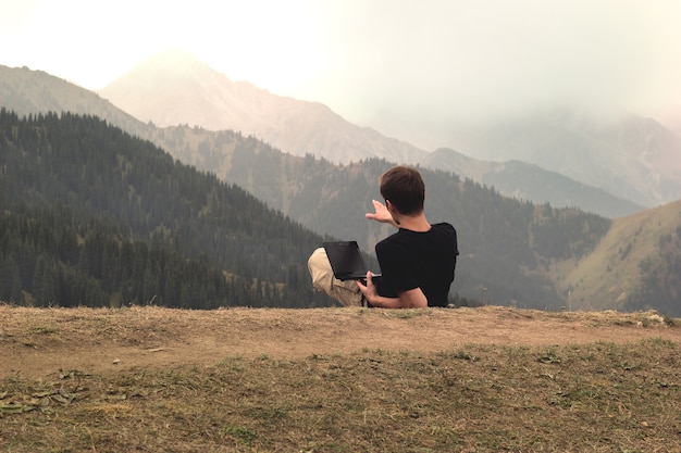 Jeune homme indépendant allongé et travaillant avec un ordinateur portable dans les montagnes.