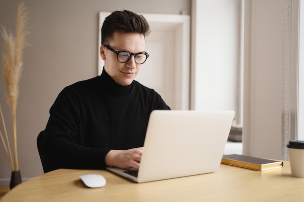 Un jeune homme indépendant travaillant sur un lieu de travail utilise un ordinateur portable pour imprimer un message texte en ligne