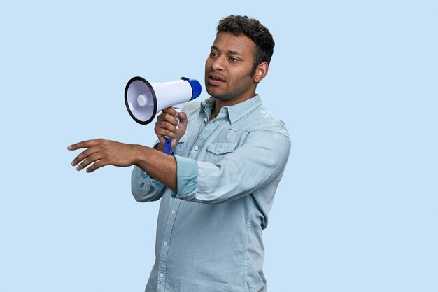 Jeune homme indien ou arabe brun parlant dans un mégaphone isolé sur fond bleu pâle