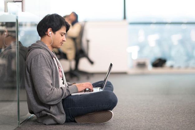 jeune homme indien développeur de logiciels utilisant un ordinateur portable écrivant du code de programmation alors qu'il était assis par terre dans un bureau de démarrage créatif moderne