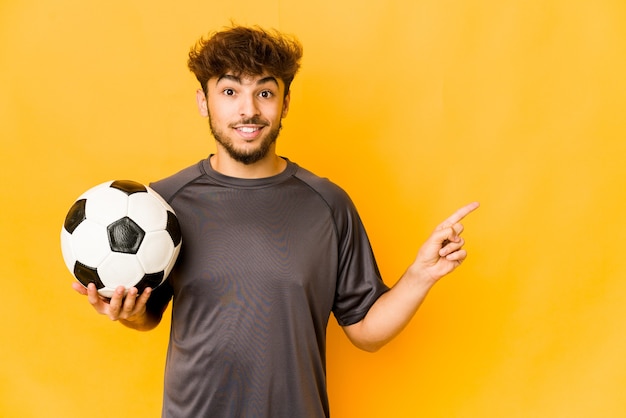 Jeune homme indien de footballeur souriant et pointant de côté, montrant quelque chose à l'espace vide.