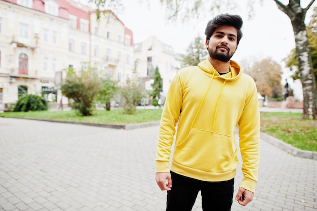 Jeune homme indien hipster urbain dans un sweat-shirt jaune à la mode Cool mec sud-asiatique porter un sweat à capuche marcher dans la rue