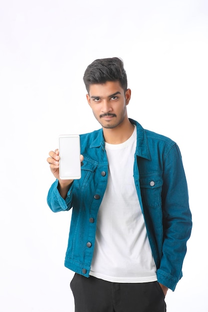 Jeune homme indien montrant l'écran du smartphone sur fond blanc.