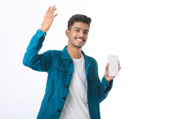 Jeune homme indien montrant l'écran du smartphone sur fond blanc.