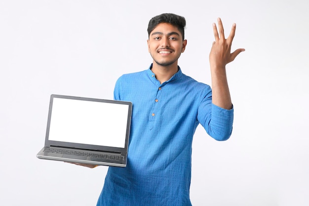 Jeune homme indien montrant un écran d'ordinateur portable sur fond blanc.