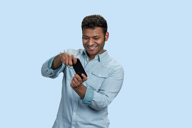 Jeune homme indien souriant jouant au jeu vidéo sur téléphone mobile isolé sur fond bleu pastel