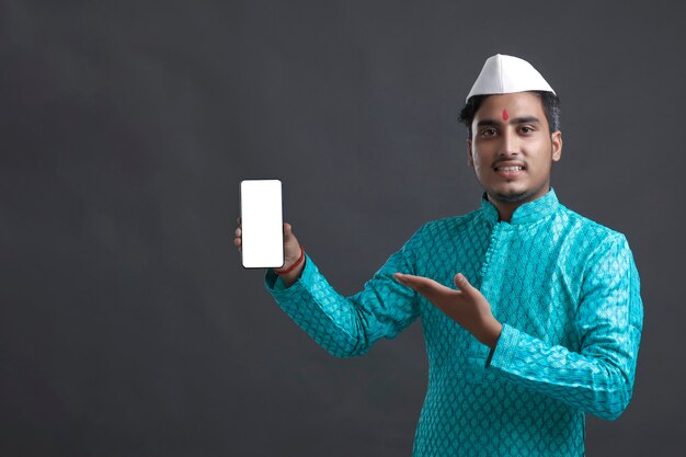 Jeune homme indien en tenue traditionnelle et montrant un smartphone.