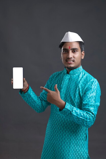 Jeune homme indien en tenue traditionnelle et montrant un smartphone.