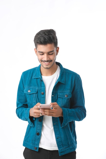 Jeune homme indien utilisant un smartphone et donnant une expression sur fond blanc.