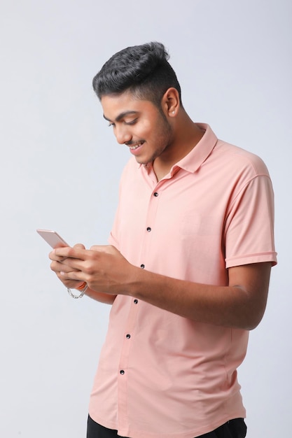 Jeune homme indien utilisant un smartphone et donnant une expression sur fond blanc.