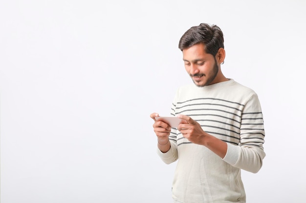 Jeune homme indien utilisant un smartphone et donnant une expression sur fond blanc.