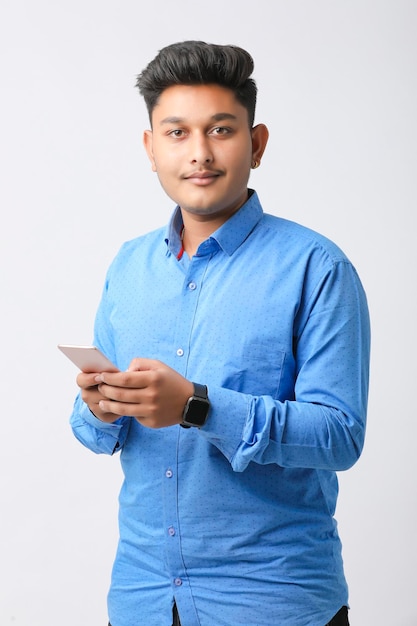 Jeune homme indien utilisant un smartphone et donnant une expression sur fond blanc.