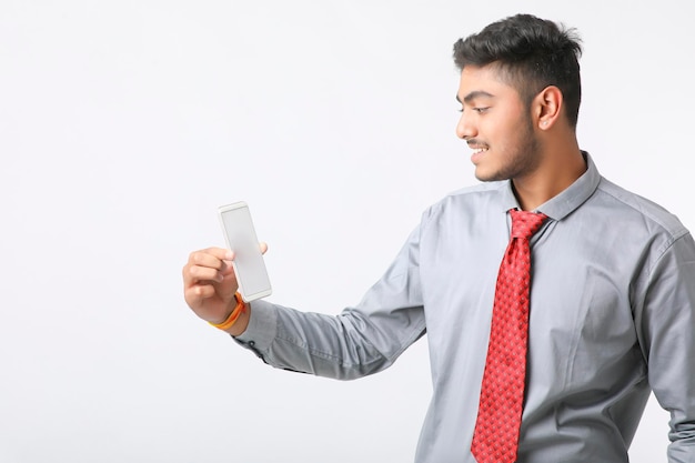 Jeune homme indien utilisant un smartphone et donnant une expression sur fond blanc.