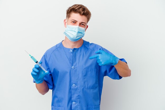 Jeune homme infirmier caucasien prêt à donner un vaccin isolé sur mur blanc personne pointant à la main vers un espace de copie de chemise, fier et confiant