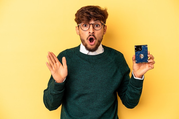 Jeune homme informaticien isolé sur fond jaune surpris et choqué.