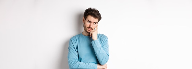 Jeune homme inquiet avec barbe en sweat-shirt regardant loin pensif et pensant à nouveau troublé