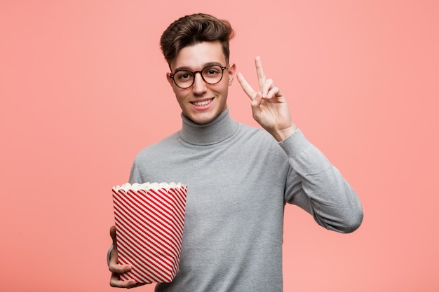 Jeune homme intellectuel tenant un seau à pop-corn à côté avec une expression douteuse et sceptique.