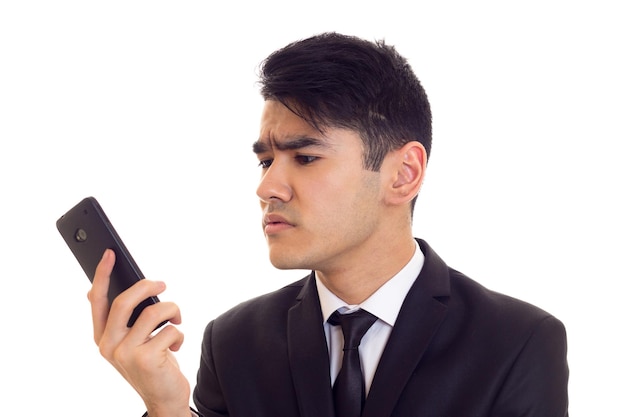 Jeune homme intelligent aux cheveux noirs en chemise blanche et costume noir avec cravate à l'aide de son téléphone