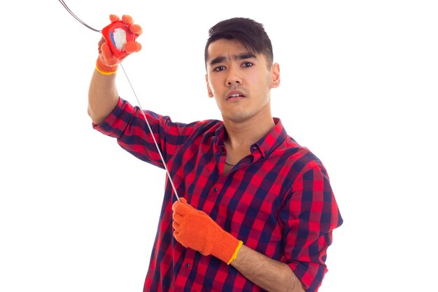 Jeune homme intelligent aux cheveux noirs en chemise à carreaux rouge avec des gants orange tenant un ruban à mesurer