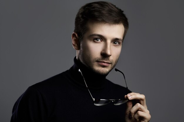 Jeune homme intelligent portant un col roulé et des lunettes sur fond gris