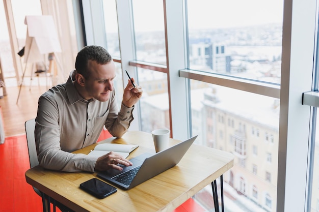 Jeune homme intelligent à la recherche d'informations sur un site Web et travaillant en tant que pigiste sur le développement d'un projet graphique sur un ordinateur portable moderne à l'aide d'une connexion Internet sans fil à l'intérieur d'un café