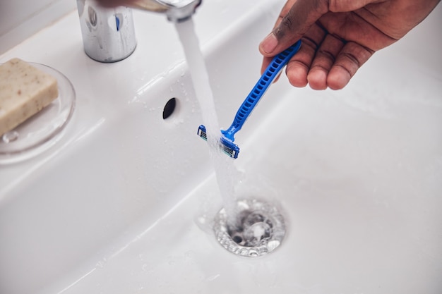 Jeune homme international debout près de l'évier et préparant un instrument stérile pour se raser la barbe