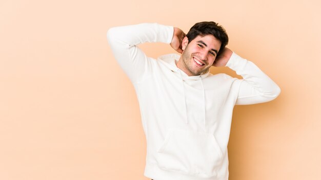 Jeune homme isolé sur beige étirement des bras, position détendue.