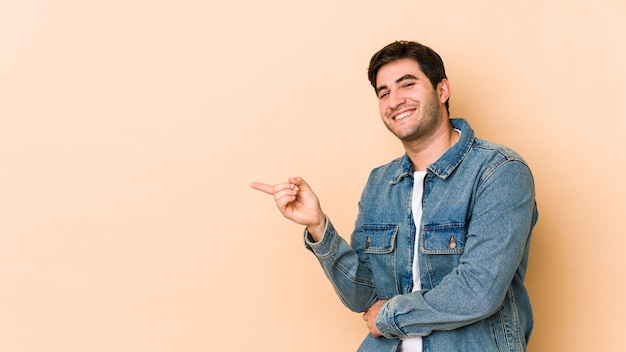 Jeune homme isolé sur beige pointant vers l'extérieur