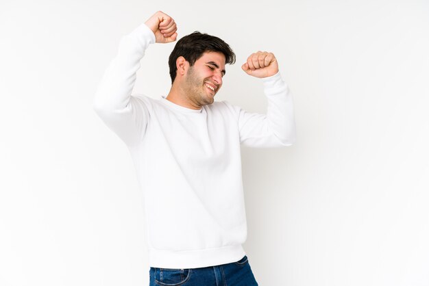 Jeune homme isolé sur blanc célébrant une journée spéciale, saute et lève les bras avec énergie.