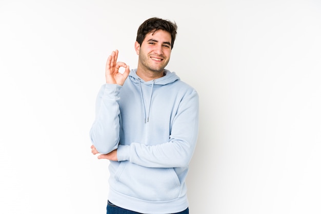 Jeune homme isolé sur blanc fait un clin d'œil et détient un geste correct avec la main.