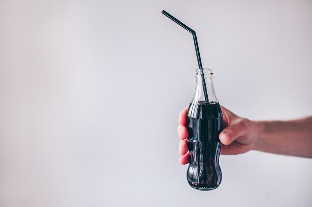 Jeune homme isolé sur fond. main d'homme tenant une bouteille avec du coke à l'intérieur et de la paille en plastique. Boisson sucrée sucrée.