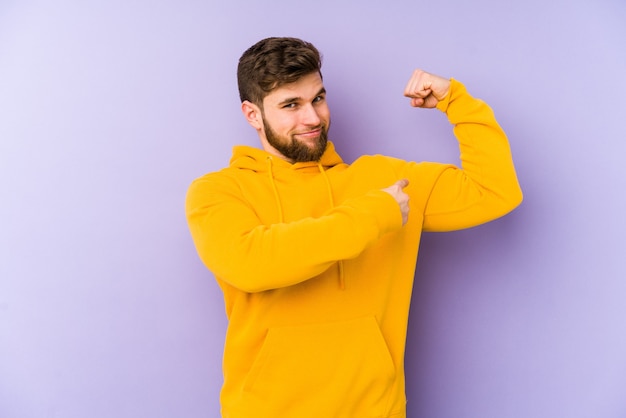 Jeune homme isolé sur fond violet montrant le geste de force avec les bras, symbole du pouvoir féminin