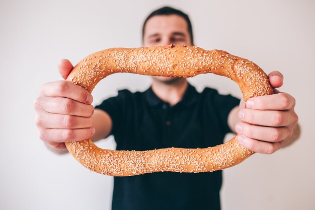 Jeune homme isolé. Guy tient chignon rond avec les mains et montre-le à la caméra. Homme en vêtements décontractés avec délicieux pain délicieux sur photo.