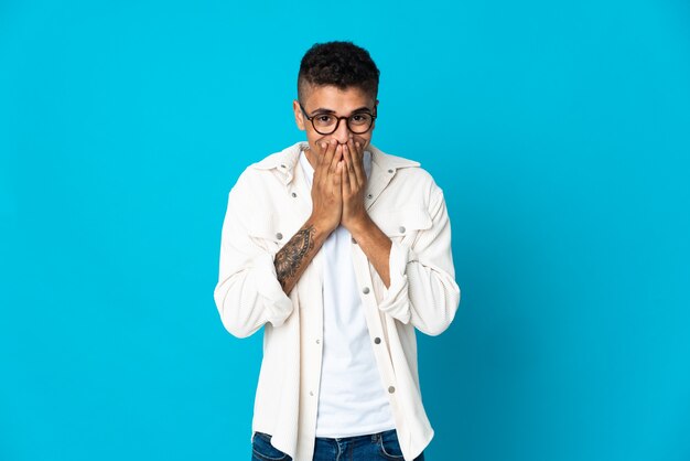 Jeune homme isolé heureux et souriant couvrant la bouche avec les mains