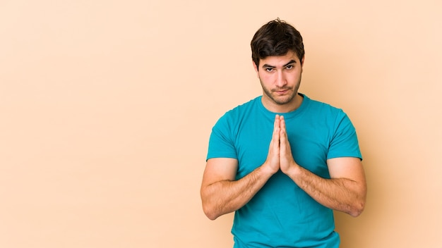 Jeune homme isolé sur un mur beige priant, montrant la dévotion, personne religieuse à la recherche d'inspiration divine.