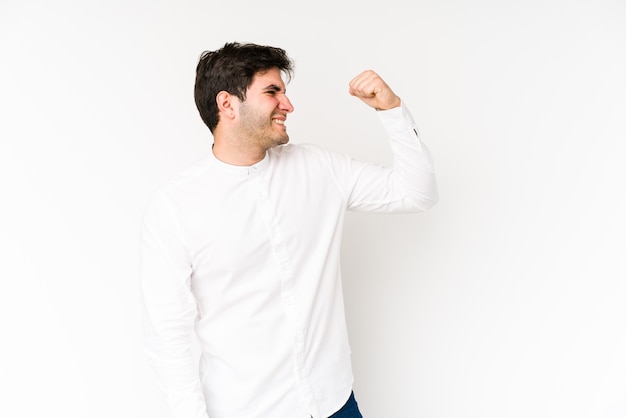 Jeune homme isolé sur un mur blanc célébrant une victoire, passion et enthousiasme, expression heureuse.