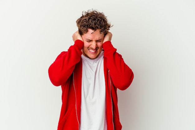 Jeune homme isolé sur un mur blanc couvrant les oreilles avec les mains en essayant de ne pas entendre un son trop fort