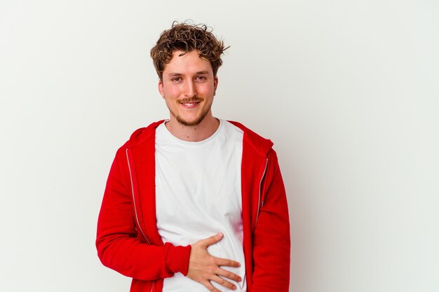 Jeune homme isolé sur un mur blanc touche le ventre, sourit doucement, concept de manger et de satisfaction