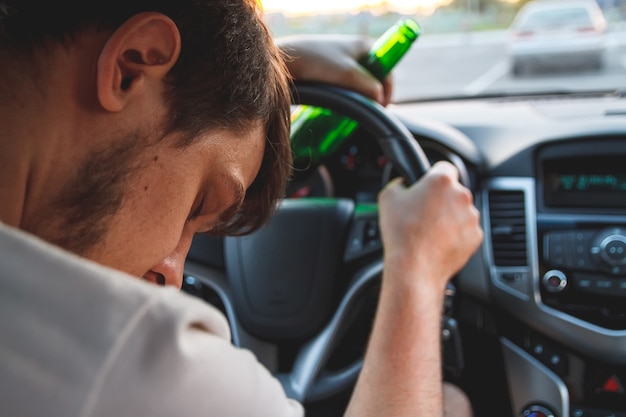 Jeune homme ivre conduisant une voiture avec une bouteille de bière