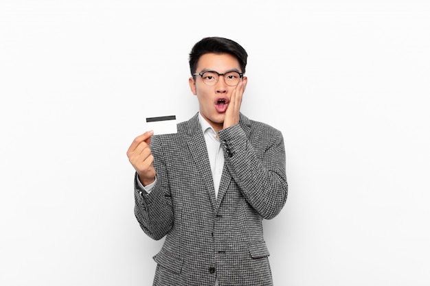 Jeune homme japonais se sentant choqué et effrayé, l'air terrifié avec la bouche ouverte et les mains sur les joues. concept de carte de crédit.