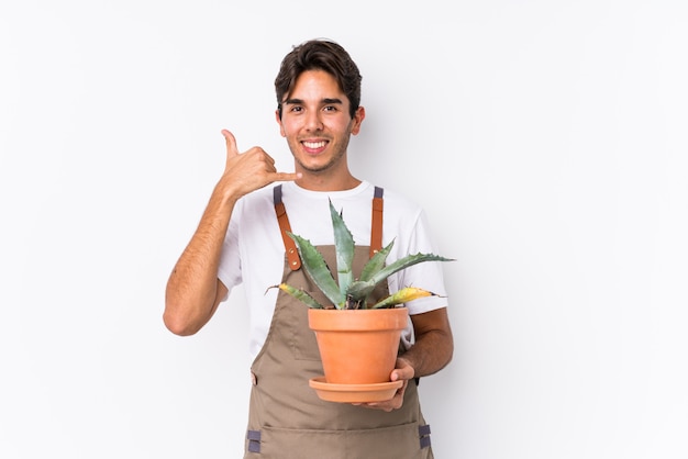 Jeune homme jardinier caucasien tenant une plante isolée montrant un geste d'appel de téléphone mobile avec les doigts.