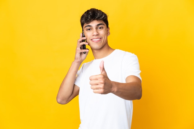 Jeune homme sur jaune en gardant une conversation avec le mobile tout en faisant les pouces vers le haut