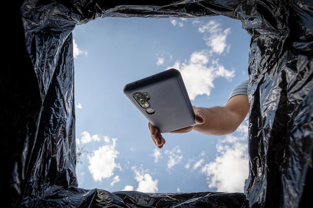 Jeune homme jetant un smartphone dans une poubelle à l'extérieur Recyclage d'un smartphone cassé