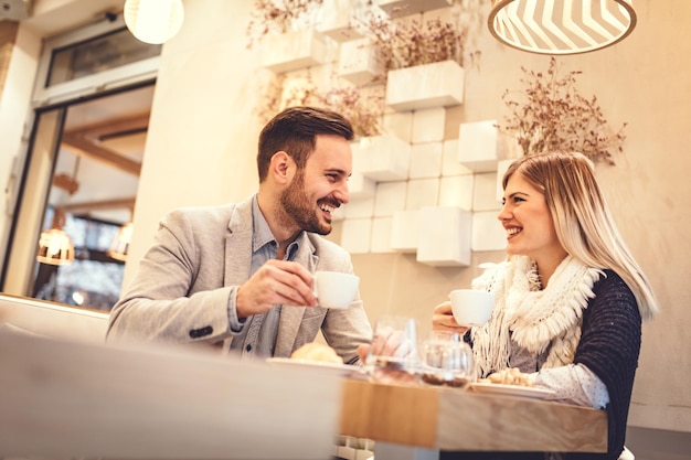 Jeune homme et jeune femme assise au café et parler avec le sourire. Ils boivent du café et prennent leur petit déjeuner.