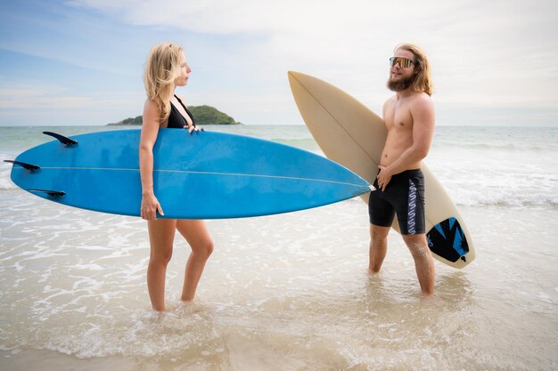 Un jeune homme et une jeune femme tenant des planches de surf prêts à marcher dans la mer pour surfer