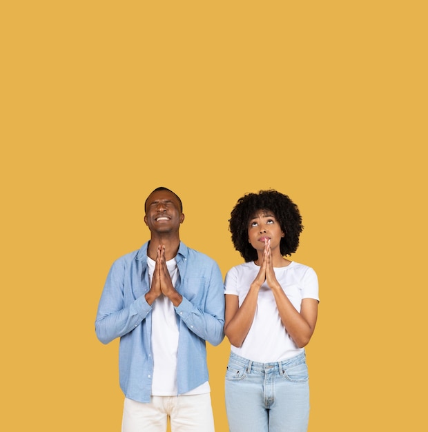 Un jeune homme et une jeune femme en tenue décontractée se tiennent les yeux fermés et les mains jointes.