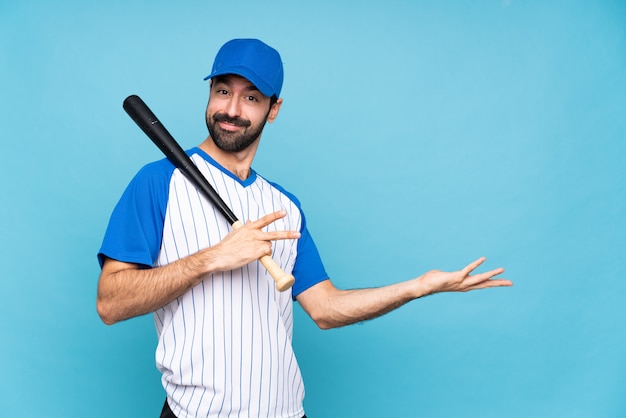 Jeune homme jouant au baseball sur bleu isolé s'étendant les mains sur le côté pour inviter à venir