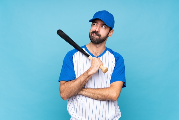 Jeune homme jouant au baseball sur mur bleu isolé avec une expression du visage confuse