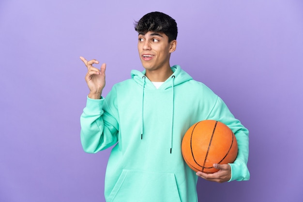 Jeune homme jouant au basket-ball sur fond violet isolé dans l'intention de réaliser la solution tout en levant un doigt