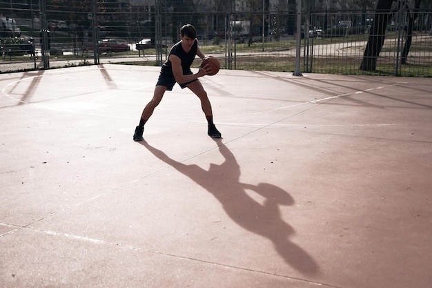 Jeune homme jouant au basketball en plein air dans la rue avec de longues ombres